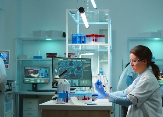 Medical lab worker analyzing blood serum conducting virus test in modern equipped lab late at night. Team of specialists examining vaccine evolution using high tech for treatment against covid19
